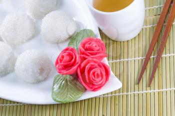 Top view horizontal angled image of Chinese sweet sticky rice balls, in background, red decoration roses, and green tea with natural bamboo place mat 