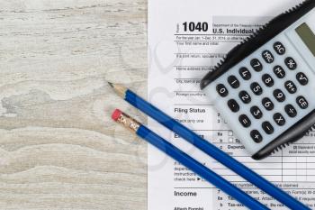 U.S. Tax form 1040 with calculator and pencils on wooden desktop 