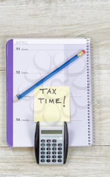 Vertical top view of an office wooden desktop with small calendar, calculator and sharpen blue pencil with reminder of doing Tax Return. 