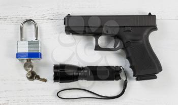 Overhead angled view of security items consisting of pistol, flashlight, and padlock with keys on white desktop. 