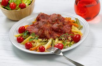 Freshly cooked pasta, meatballs in thick sauce, cherry tomatoes, parsley, red wine and salad with white wood underneath. 