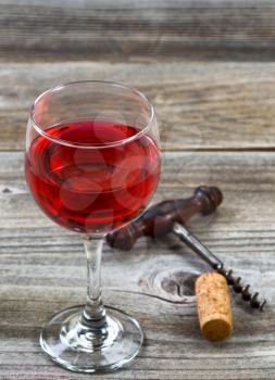 Vertical image of red wine, focus on front lip of glass, with antique corkscrew and cork in background on rustic wood. 