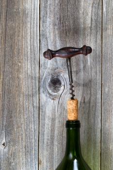 Vertical image of antique corkscrew pulling out cork in wine bottle on rustic wood. 
