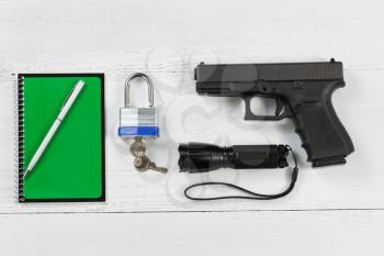 Overhead angled view of security items consisting of pistol, flashlight, pen, notepad and padlock with keys on desktop. 