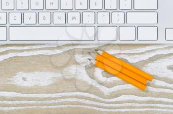 Office desktop with three pencils and keyboard on aged white wood. Top view angled shot in horizontal format with copy space.     