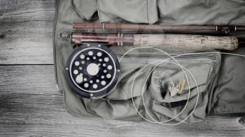 Vintage concept of an antique fly fishing reel and rod with vest and flies on rustic wood. Layout in horizontal format.