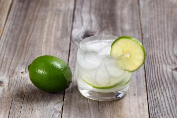 Lime drink, focus on lip of glass and lime slice, with whole lime on rustic wood. 