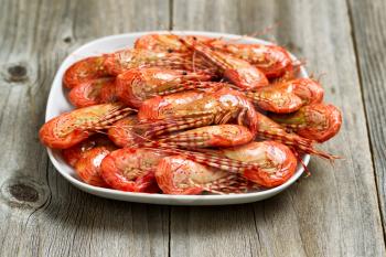 Close up image of freshly steamed shrimp in white plate on top of rustic wood. Layout in horizontal format. 
