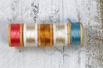 Top view of colorful spools of thread on rustic white wood. Layout in horizontal format. 