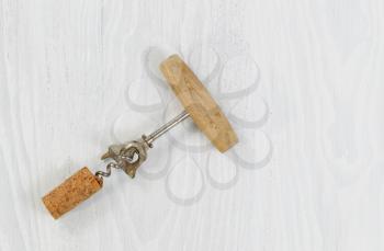 Top view of an antique corkscrew with cork attached on white wood.

