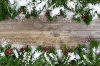 Christmas border, top and bottom of frame, with pine tree branches, cones and snow on rustic wooden boards. Layout in horizontal format.  