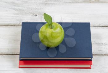 A healthy green apple on top of books with rustic white wood in background. Education concept of back to school.