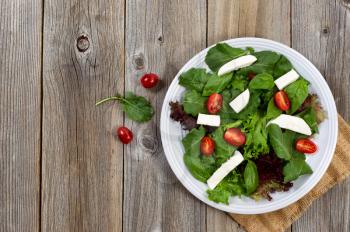 Fresh salad with cheese, cherry tomato, basil, baby kale, and lettuce on rustic wood. 