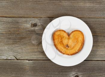Single heart shaped cookie on white plate with rustic wood in background.