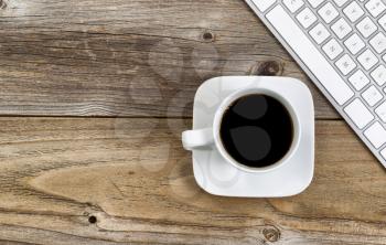 Top view of black coffee, selective focus on upper lip of coffee cup, with partial computer keyboard on rustic wood.