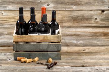 Red wine bottles in wooden crate with old corkscrew and used corks on rustic wooden boards. 