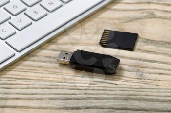 Close up of data thumb drive and memory flash card. Computer keyboard in background on desktop. 