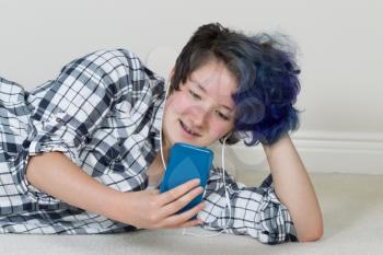 Teen girl looking at cell phone while lying down listening to music at home. Layout in horizontal format. 