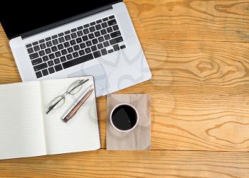 Top view of computer laptop with dark coffee, notepad, reading glasses and pens on desktop. 