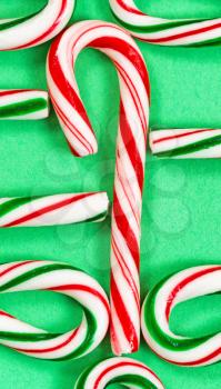 Single red and white candy cane joining with a collection of partial candy canes on green background. Layout in vertical format. 