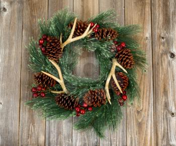 Western style wreath with antlers, pine cones and berries on rustic wood. Boards in vertical layout. 