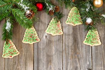 High angled view of tree shaped cookies with evergreen branches, pine cones, snow and ornaments on rustic wood. 