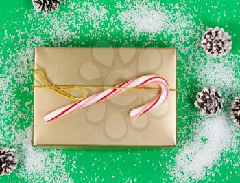 High angle shot of golden gift box, candy cane and pine cones on light snowy green background. 
