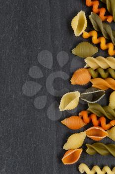 Colorful raw pasta on natural black slate stone.  Vertical layout.