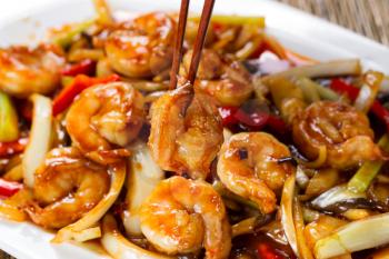 Close up front view of a curry shrimp, selective focus on single piece in chopsticks, with fresh peppers on onion in background. 