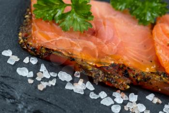 Close up of finely sliced smoked salmon, tilted angle, on natural slate stone with coarse salt. Selective focus on front part of salmon. 