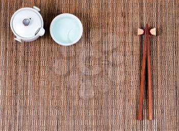 Overhead view of chopsticks, cup and tea server on bamboo mat.  