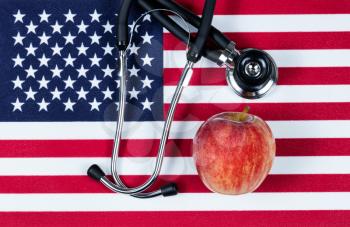 United States of America flag with stethoscope and red apple. USA health concept. Overhead view in horizontal layout.