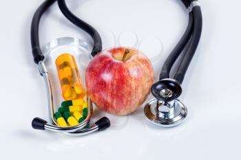 Red apple, medicine capsules and stethoscope on white table with reflection. Good health care concept. 