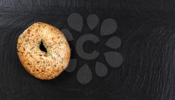 Overhead view of freshly baked seeded bagel on natural slate stone. 