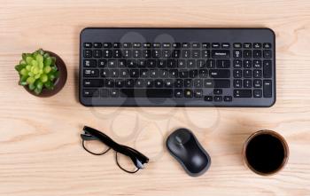 Overhead view of a clean desk consisting of computer keyboard, baby plant, mouse, coffee, and reading glasses. 