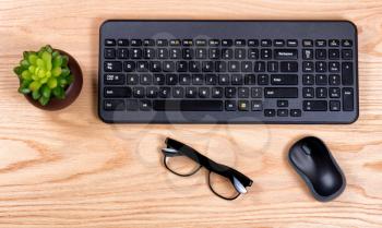 Overhead view of a clean desk consisting of computer keyboard, baby plant, mouse, and reading glasses. 