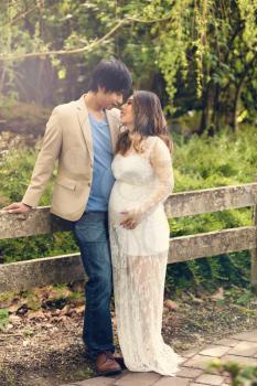 Expecting mom and dad leaning against split rail fence in the woods. Haze light effect applied to image.    