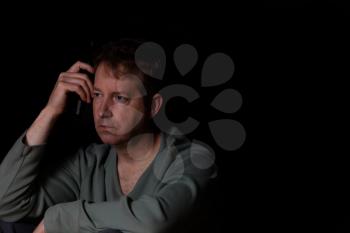 Depressed man holding bottle of beer against his head while in thought. Dark background. 