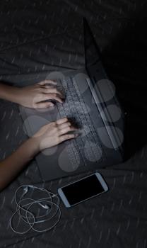 Hands typing on computer while at nighttime in bed. Light effect on hands and computer keyboard. 