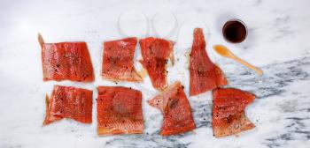 Overhead view of a raw red salmon fillets with seasonings and maple syrup on natural marble stone counter. Preparing fish for smoke cooking. 