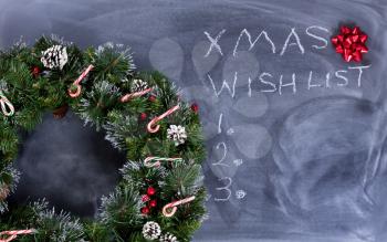Wreath, gift bow and candy canes on erased chalkboard with Christmas wish list written on board. 