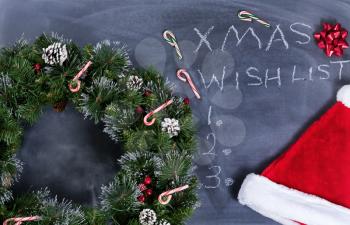 Holiday Wreath, Santa cap, gift bow and candy canes on erased chalkboard with Christmas wish list written on board. 