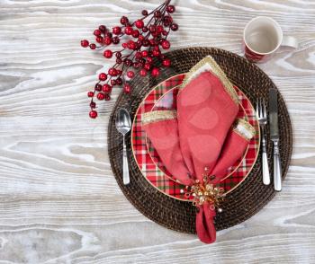Overhead view of a festive Christmas dinner setting with red berry decorations on top of white wood 