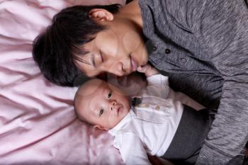 Father falls asleep before his infant baby boy while lying on the bed 