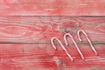 Rustic red wooden background for Christmas concept with three candy canes. Overhead view with copy space.