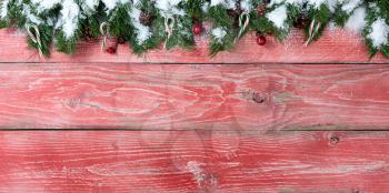 Rustic red wooden background for Christmas concept with snowy fir branches, candy canes, red berries and pine cones. Overhead view with copy space.