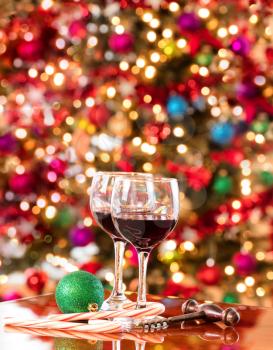 Red wine on Mahoney table with bright Christmas tree lights in background.  Vertical format layout. 
