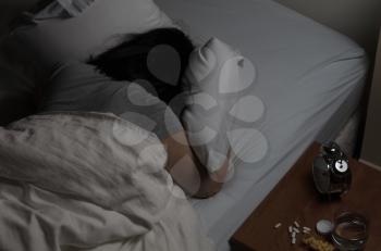 Woman planting face in pillow with pills spilled on night stand. Depression and addiction concept. 