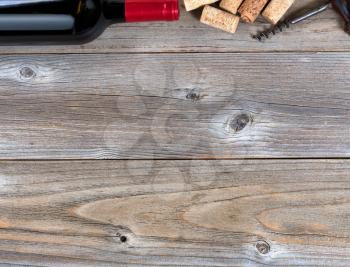 Overhead view of a top border of partial red wine bottle, corks and vintage corkscrew on rustic wood
