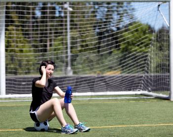 Teen age girl resting while on the soccer field during bright hot day 